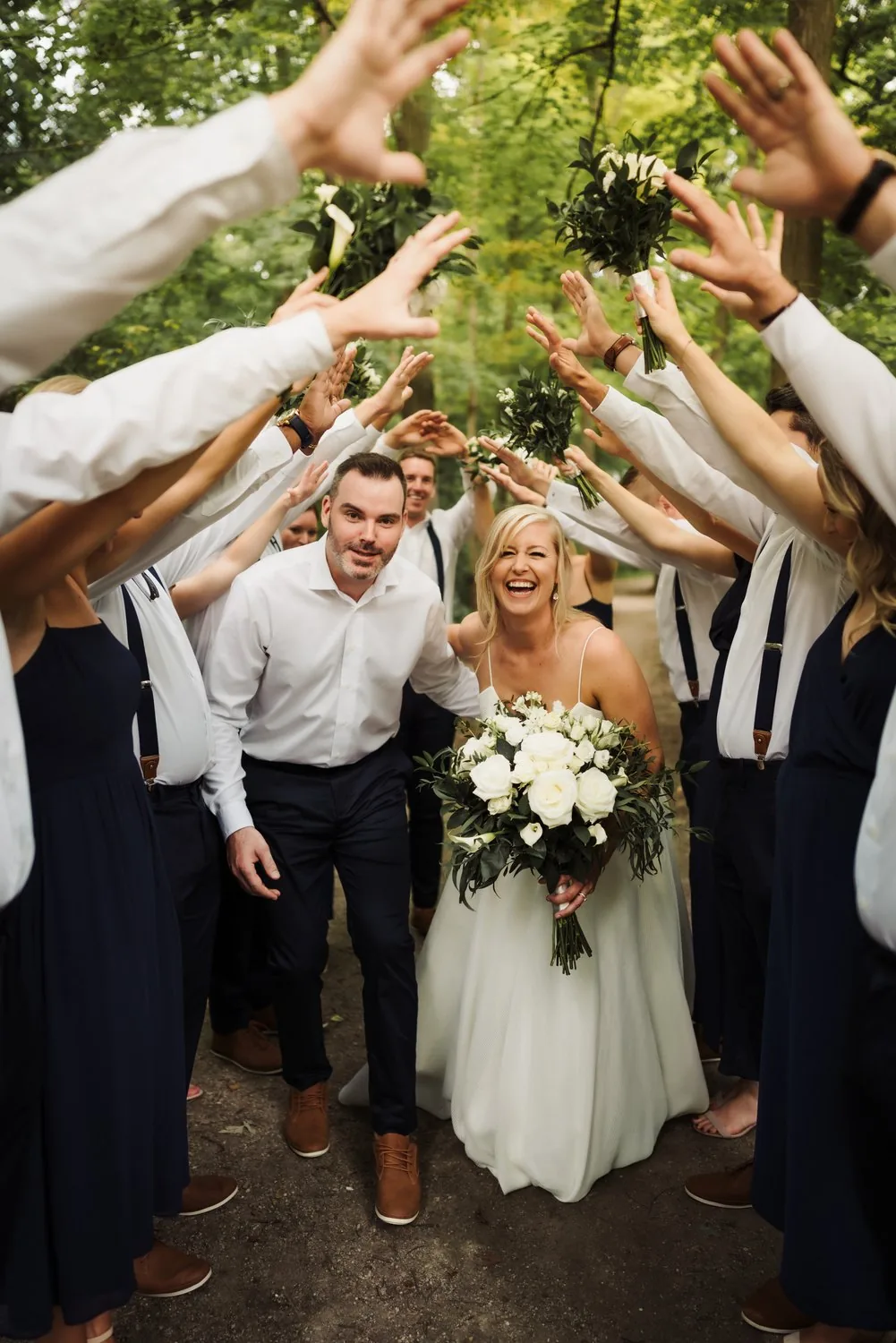 Wedding party in navy forming a tunnel of raised arms as the couple celebrates at their backyard wedding near Kitchener, Ontario