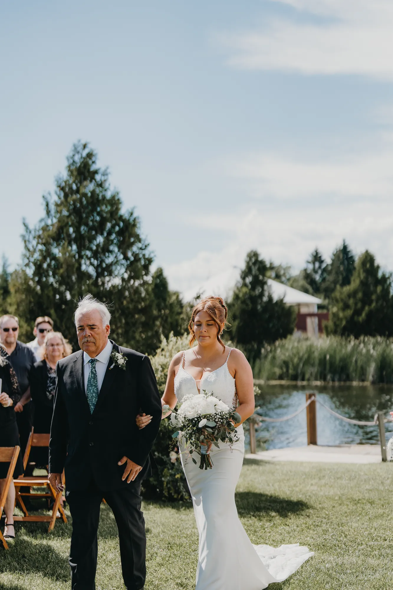 Bride walking down the aisle with her father beside the pond at The Eddie