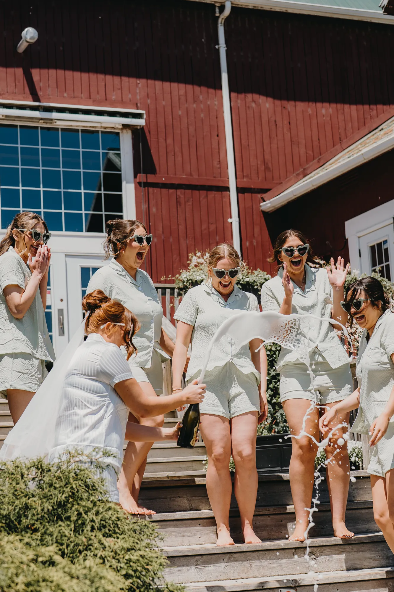 Bridesmaids in matching pajamas popping champagne on the barn steps