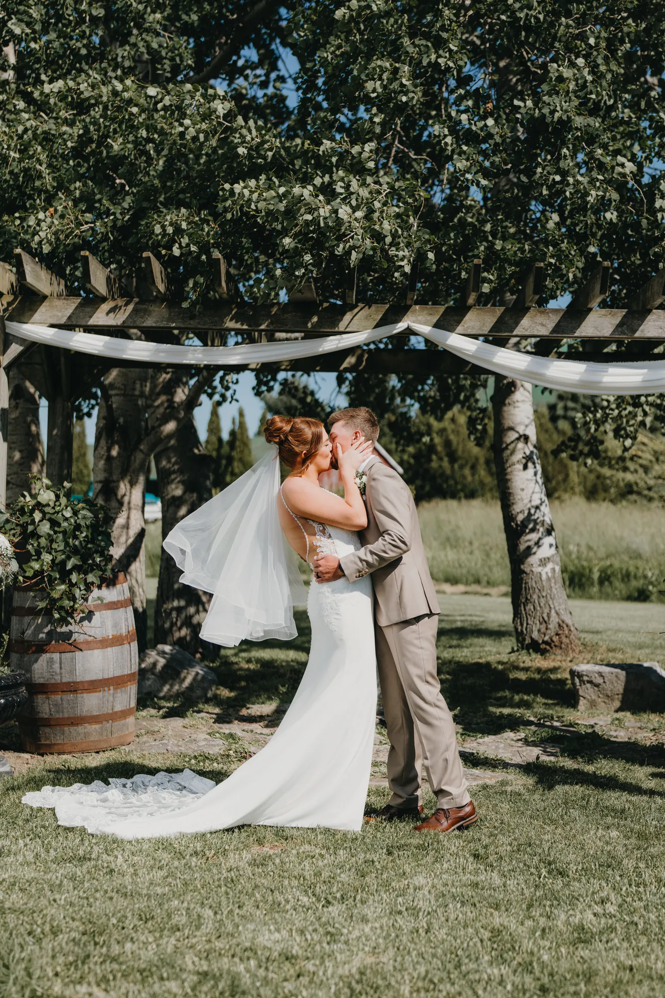 Bride and groom's first kiss under the pergola with veil blowing in the wind