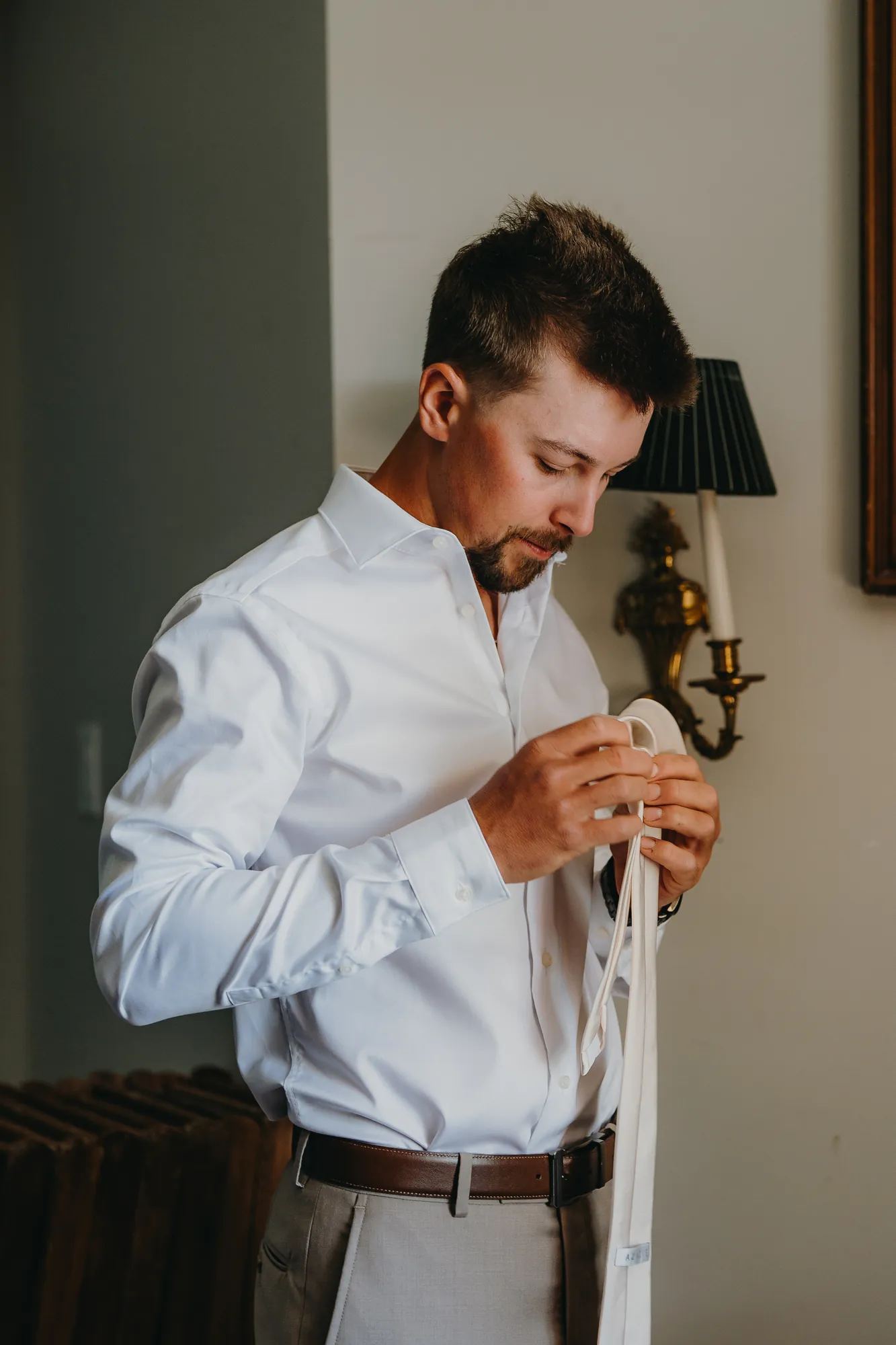 Groom tying his tie while getting ready indoors