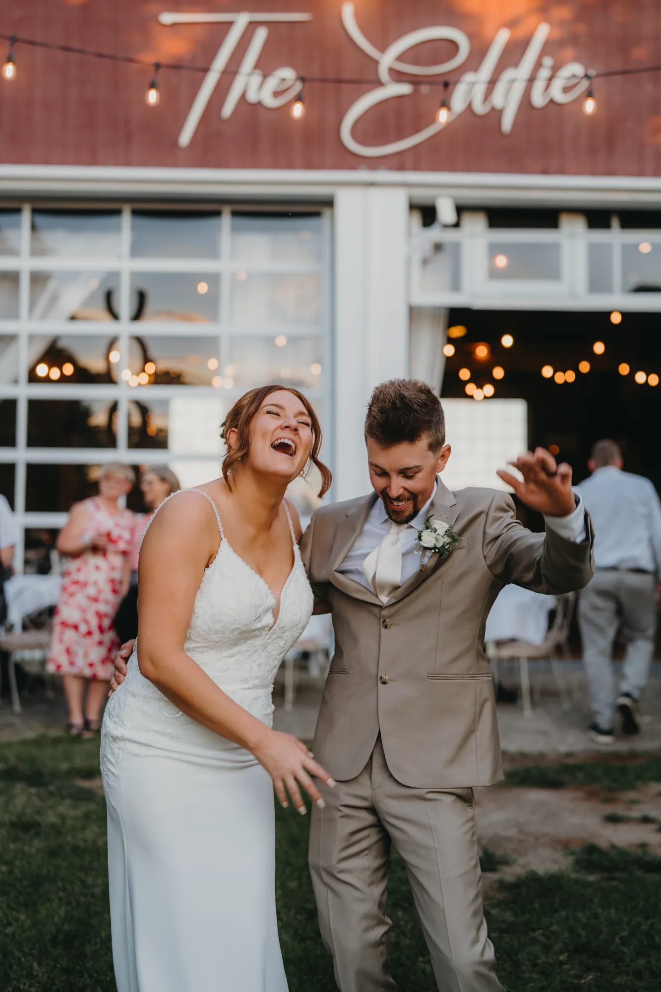Bride and groom laughing and dancing outside the barn at dusk