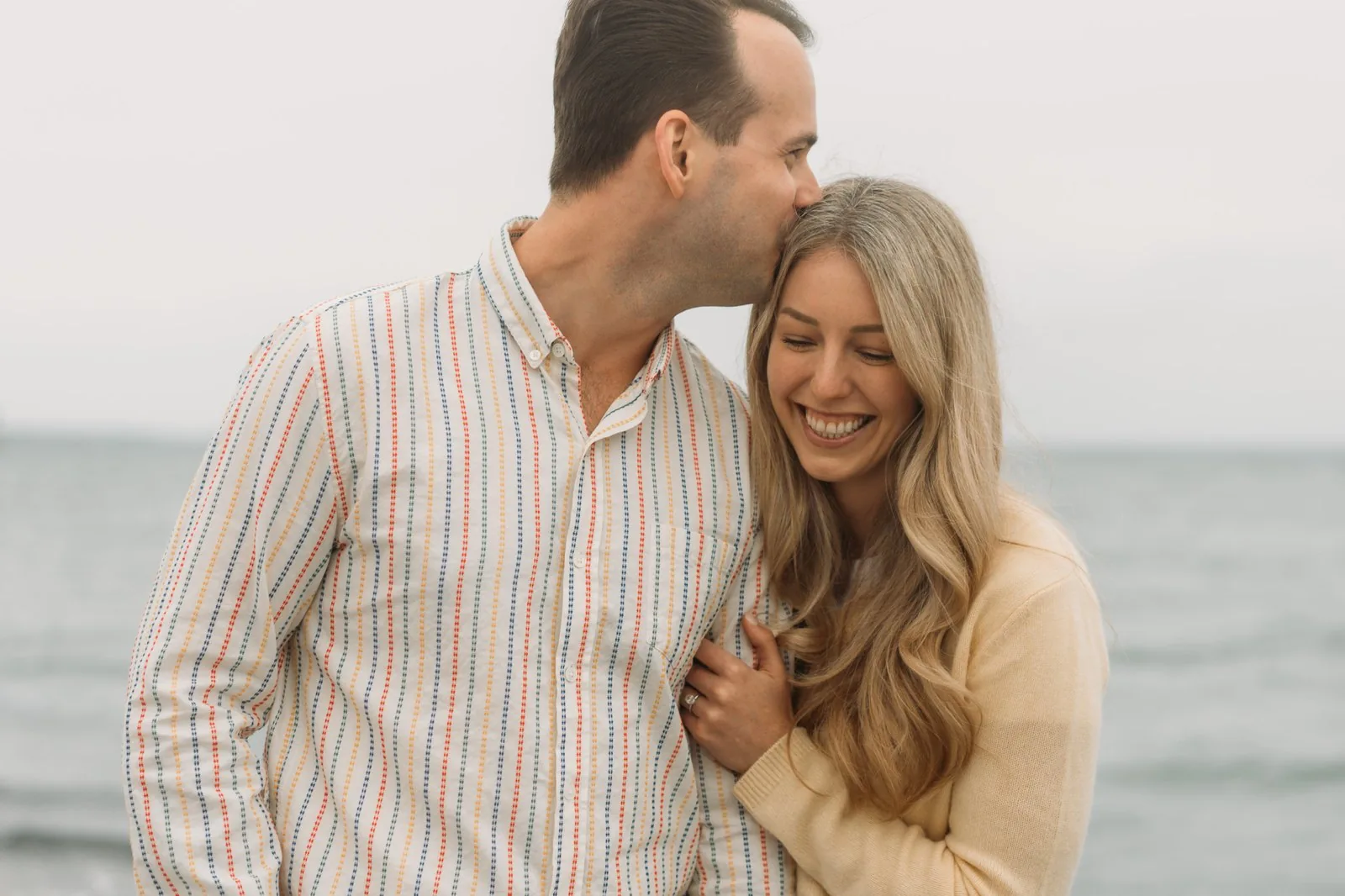 Engaged couple laughing together on the beach at the lake's edge