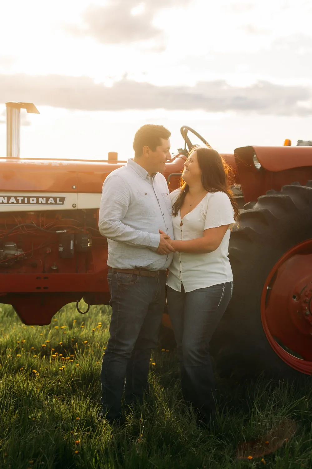 Engaged couple beside a vintage red tractor at sunset on a farm